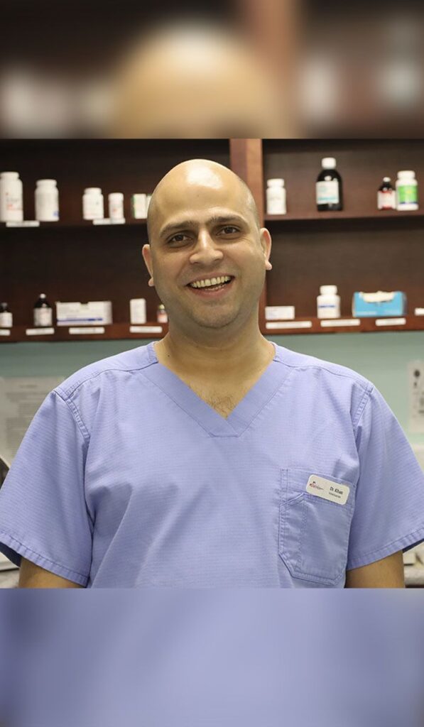 Bald man in blue scrubs smiling in a pharmacy.