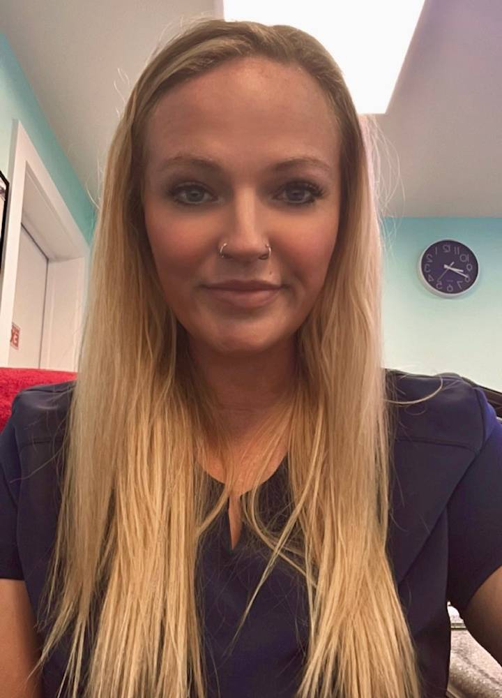 Woman with long blonde hair and a nose ring, wearing a blue top, smiling at the camera.