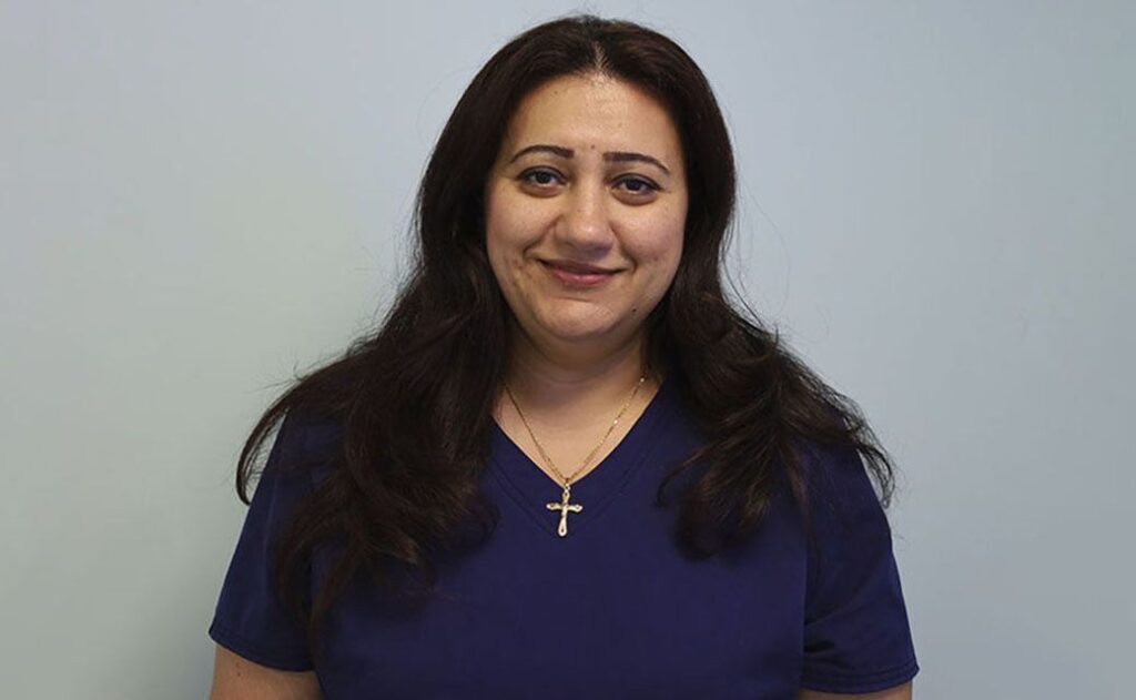 Woman in blue top with cross pendant smiling at the camera.
